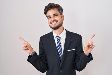 Young hispanic man with tattoos wearing business suit and tie smiling confident pointing with fingers to different directions. copy space for advertisement
