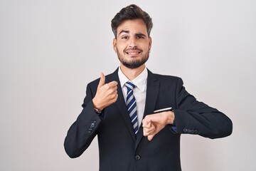 Young hispanic man with tattoos wearing business suit and tie doing thumbs up and down, disagreement and agreement expression. crazy conflict