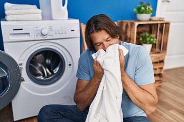 Middle age man washing clothes smelling towel at laundry room