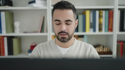 Young hispanic man student using computer studying at library university