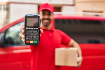 Young hispanic man courier holding package and data phone at street