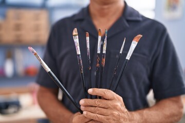 Middle age man artist holding paintbrushes at art studio