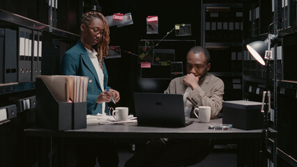 African american agents reading statements reports in incident room, trying to find suspect with surveillance footage. Private detectives examining forensic evidence on detective map, crime case.