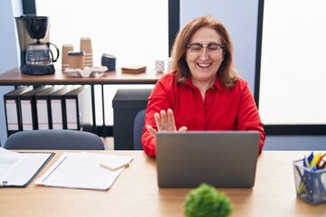 Senior woman with glasses working at the office with laptop looking positive and happy standing and smiling with a confident smile showing teeth