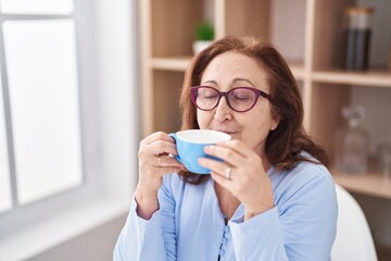 Senior woman drinking coffee sitting on table at home