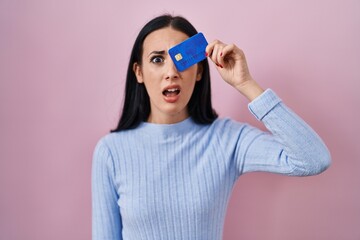 Hispanic woman holding credit card over eye clueless and confused expression. doubt concept.