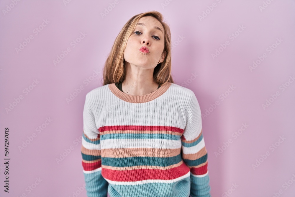 Wall mural young blonde woman standing over pink background looking at the camera blowing a kiss on air being l