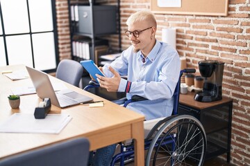 Young caucasian man business worker using touchpad sitting on wheelchair at office