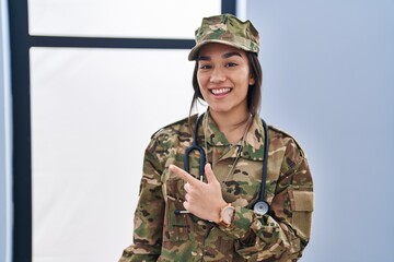 Young south asian woman wearing camouflage army uniform and stethoscope smiling cheerful pointing with hand and finger up to the side