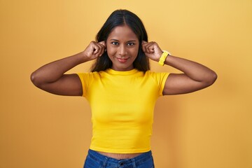 Young indian woman standing over yellow background smiling pulling ears with fingers, funny...