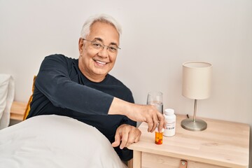Senior man taking pills treatment sitting on bed at bedroom
