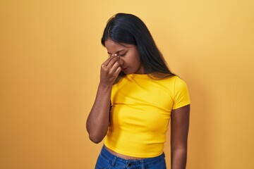 Young indian woman standing over yellow background tired rubbing nose and eyes feeling fatigue and...