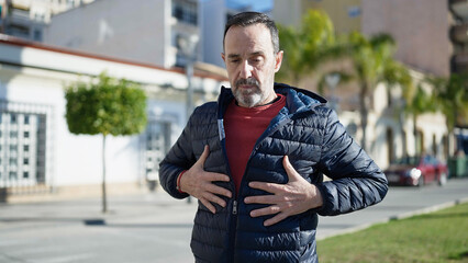 Fototapeta premium Middle age man standing with serious expression looking for something on jacket at street