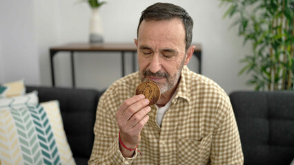 Middle age man eating cookie sitting on sofa at home