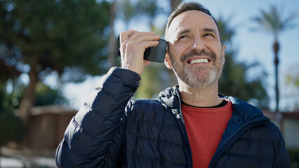 Middle age man smiling confident listening voice message by the smartphone at park