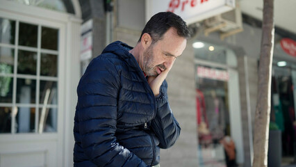 Middle age man sitting on bench with worried expression at street