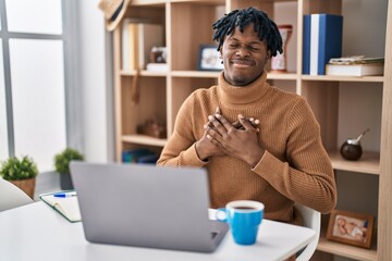 Young african man with dreadlocks working using computer laptop smiling with hands on chest with...