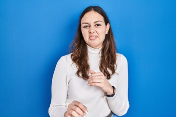 Young hispanic woman standing over blue background disgusted expression, displeased and fearful...