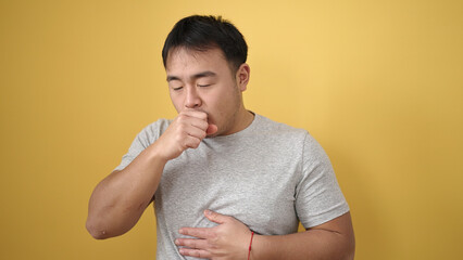 Young chinese man coughing over isolated yellow background