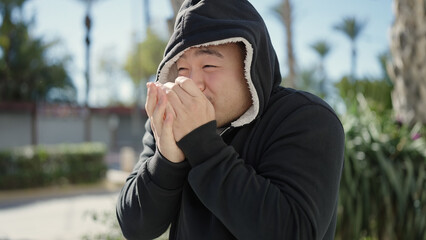 Young chinese man rubbing hands for cold wearing head with hood at park