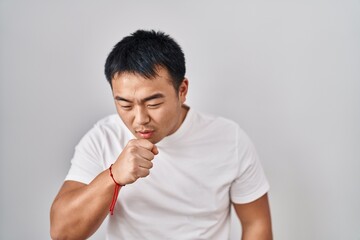 Young chinese man standing over white background feeling unwell and coughing as symptom for cold or bronchitis. health care concept.