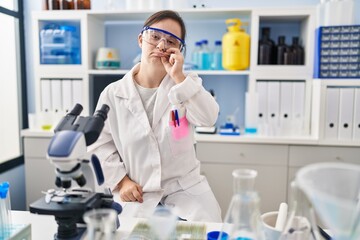 Hispanic girl with down syndrome working at scientist laboratory mouth and lips shut as zip with...