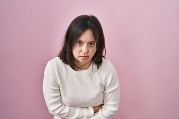 Woman with down syndrome standing over pink background with hand on stomach because indigestion,...