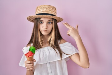 Teenager girl holding ice cream shooting and killing oneself pointing hand and fingers to head like gun, suicide gesture.