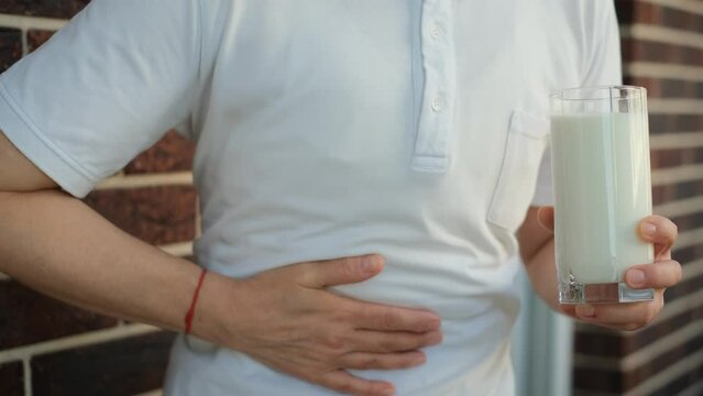 Lactose intolerance. A woman with a glass of milk holds his stomach feeling discomfort