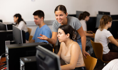 Fototapeta premium Positive female student explaining the topic to friend while she is studying computer science on the PC in the classroom.