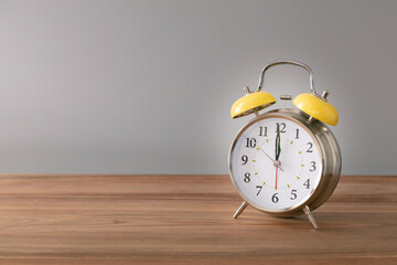 Retro silver alarm clock. 12:00.  am,  pm. Neutral background. Brown wood surface. Horizontal  photography with empty space for text or image.
