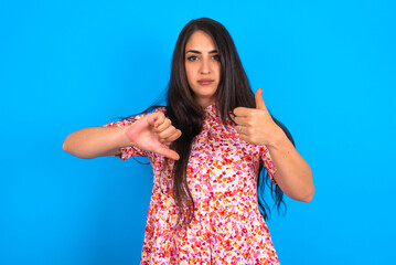 beautiful brunette woman wearing floral dress over blue background showing thumb up down sign