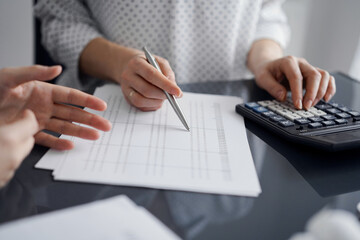 Woman accountant using a calculator and laptop computer while counting and discussing taxes with a client. Business audit and finance concepts