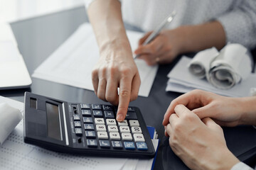 Woman accountant using a calculator and laptop computer while counting taxes for a client. Business...