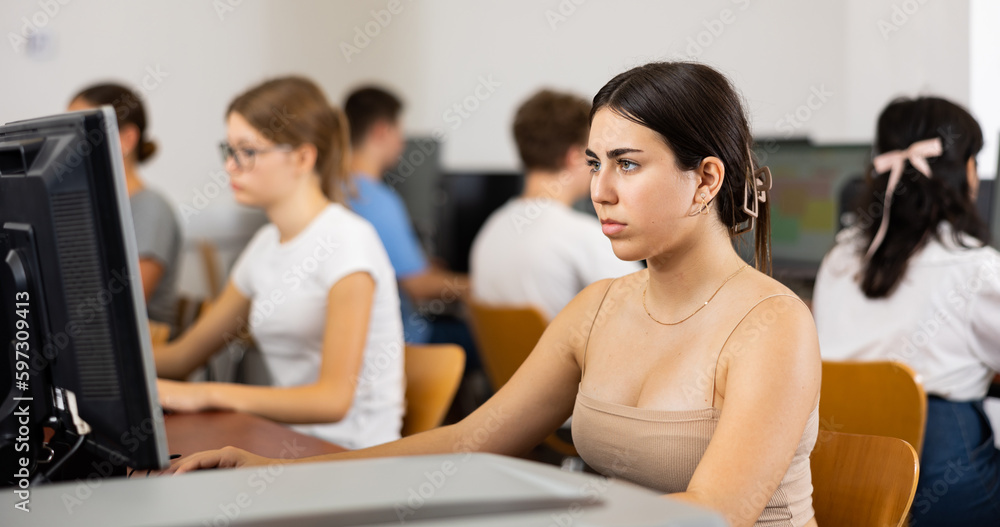 Poster smart latin female teenager learning computer science while she is using a pc in the computer classr