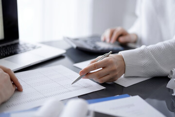 Woman accountant using a calculator and laptop computer while counting taxes for a client. Business audit concepts