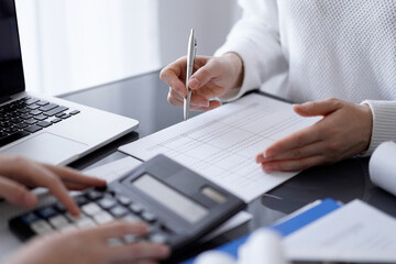 Woman accountant using a calculator and laptop computer while counting taxes for a client. Business audit concepts