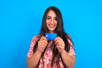 Photo of beautiful brunette woman wearing floral dress over blue background positive smile hold credit card income salary