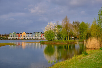 Fototapeta na wymiar Houten, The Netherlands - April 25 2023. Trees and colourful wooden lakeside houses reflected in the water of lake De Rietplas.