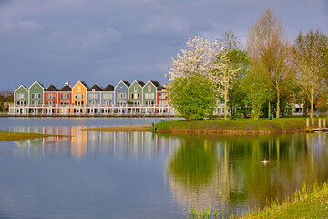Houten, The Netherlands - April 25 2023. Trees and colourful wooden lakeside houses reflected in...