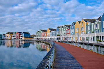 Foto auf Acrylglas Houten, The Netherlands - April 25 2023. Wooden bridge alongside colourful wooden lakeside houses. Reflected in the water of lake De Rietplas. Diminishing perspective. © Nigel Wiggins