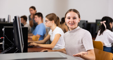 Positive female student smiling, using PC and studying computer science in the classroom