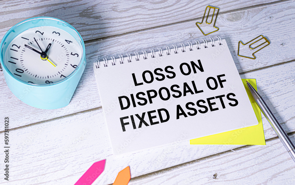 Poster loss on disposal of fixed assets label on notepad with laptop and smartphone on wooden table.