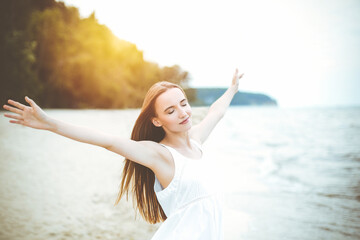 Fototapeta na wymiar Happy smiling woman in free happiness bliss on ocean beach standing with open hands. Portrait of a multicultural female model in white summer dress enjoying nature