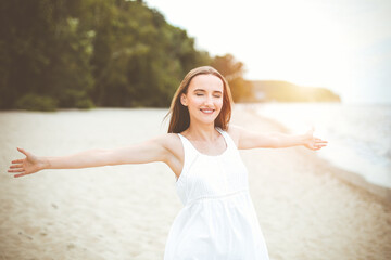 Happy smiling woman in free happiness bliss on ocean beach standing with open hands. Portrait of a multicultural female model in white summer dress enjoying nature