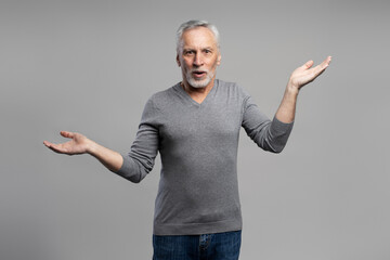 Caucasian handsome surprised gray haired bearded senior man, holding hands palms up, grey background