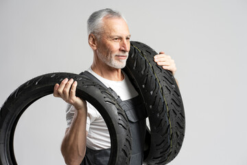 Smiling senior man mechanic technician in repair shop holding motorcycle tires on white background