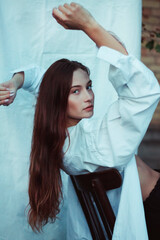 Naklejka premium Modern photo of a girl in a white shirt against a white sheet. Posing on a chair. Laconic photos of a confident woman