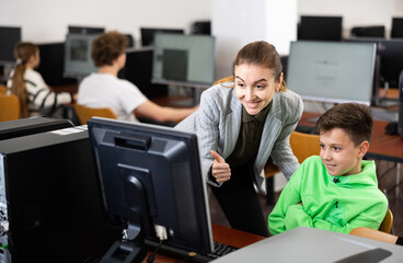 Positive female teacher tells a teenager how to work on a computer