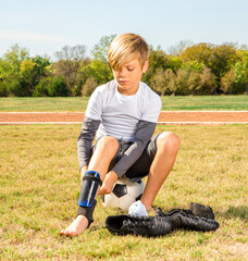 Young boy soccer player putting on his shin guards while sitting on a soccer ball © 3Days2Go Media
